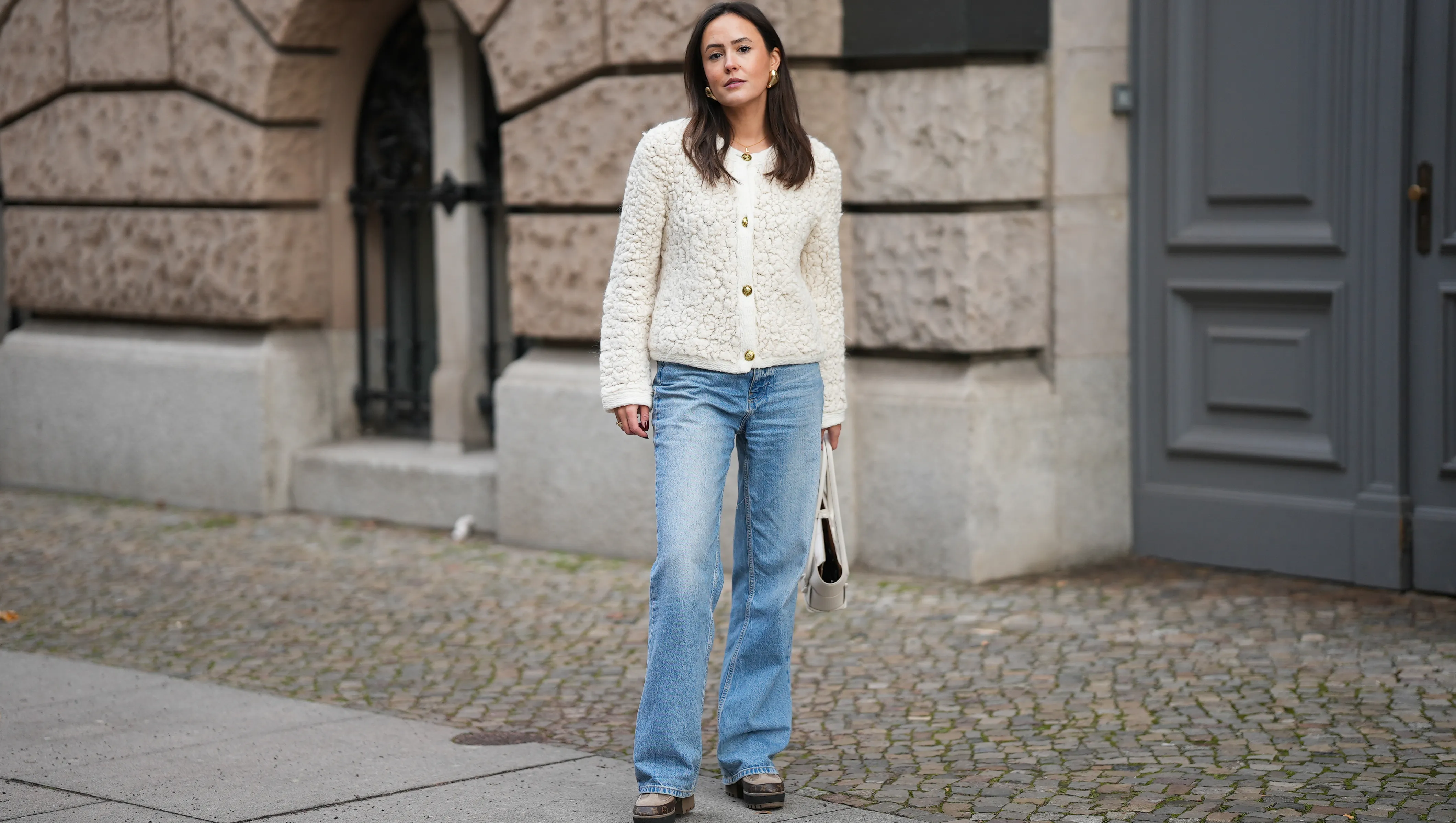 BERLIN, GERMANY - NOVEMBER 25: Laura Noltemeyer is seen wearing a cream textured boucl√© knit cardigan with a structured silhouette and gold button fastening from Massimo Dutti; light-blue straight-leg denim trousers with a soft fading in a classic cut from Zara; dark-brown and taupe monogram-detailed leather platform boots with a chunky rubber sole and suede details from Louis Vuitton; a white structured leather top-handle bag in an intrecciato weave and trapeze silhouette called ‚ÄúIntrecciato Tote‚Äù from Bottega Veneta; chunky sculptural gold earrings from Zara; her dark brown hair is worn loose, straight and parted in the middle on November 25, 2025 in Berlin, Germany. (Photo by Moritz Scholz/Getty Images)
