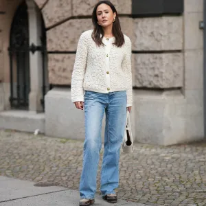 BERLIN, GERMANY - NOVEMBER 25: Laura Noltemeyer is seen wearing a cream textured bouclé knit cardigan with a structured silhouette and gold button fastening from Massimo Dutti; light-blue straight-leg denim trousers with a soft fading in a classic cut from Zara; dark-brown and taupe monogram-detailed leather platform boots with a chunky rubber sole and suede details from Louis Vuitton; a white structured leather top-handle bag in an intrecciato weave and trapeze silhouette called “Intrecciato Tote” from Bottega Veneta; chunky sculptural gold earrings from Zara; her dark brown hair is worn loose, straight and parted in the middle on November 25, 2025 in Berlin, Germany. (Photo by Moritz Scholz/Getty Images)