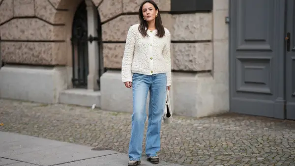 BERLIN, GERMANY - NOVEMBER 25: Laura Noltemeyer is seen wearing a cream textured bouclé knit cardigan with a structured silhouette and gold button fastening from Massimo Dutti; light-blue straight-leg denim trousers with a soft fading in a classic cut from Zara; dark-brown and taupe monogram-detailed leather platform boots with a chunky rubber sole and suede details from Louis Vuitton; a white structured leather top-handle bag in an intrecciato weave and trapeze silhouette called “Intrecciato Tote” from Bottega Veneta; chunky sculptural gold earrings from Zara; her dark brown hair is worn loose, straight and parted in the middle on November 25, 2025 in Berlin, Germany. (Photo by Moritz Scholz/Getty Images)