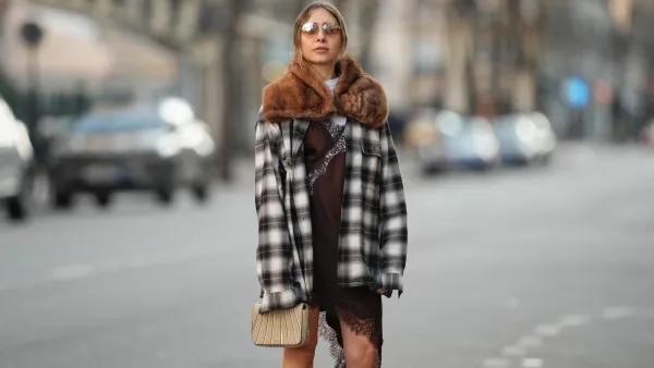 PARIS, FRANCE - DECEMBER 27: Emy Venturini wears light brown hair parted at the center and pulled back, a natural complexion with soft rose-toned lipstick, brown-tinted sunglasses by Prada, a brown faux-fur vintage scarf draped around the shoulders, a black and white plaid long-sleeve shirt by JW Anderson x Uniqlo worn open, layered over a white crew-neck cotton T-shirt by The Frankie Shop, a brown slip-style mini dress by Zara with lace trim visible at the hem, and carries a small beige structured bag by Liase, during a street style fashion photo session, on December 27, 2025 in Paris, France. (Photo by Edward Berthelot/Getty Images)
