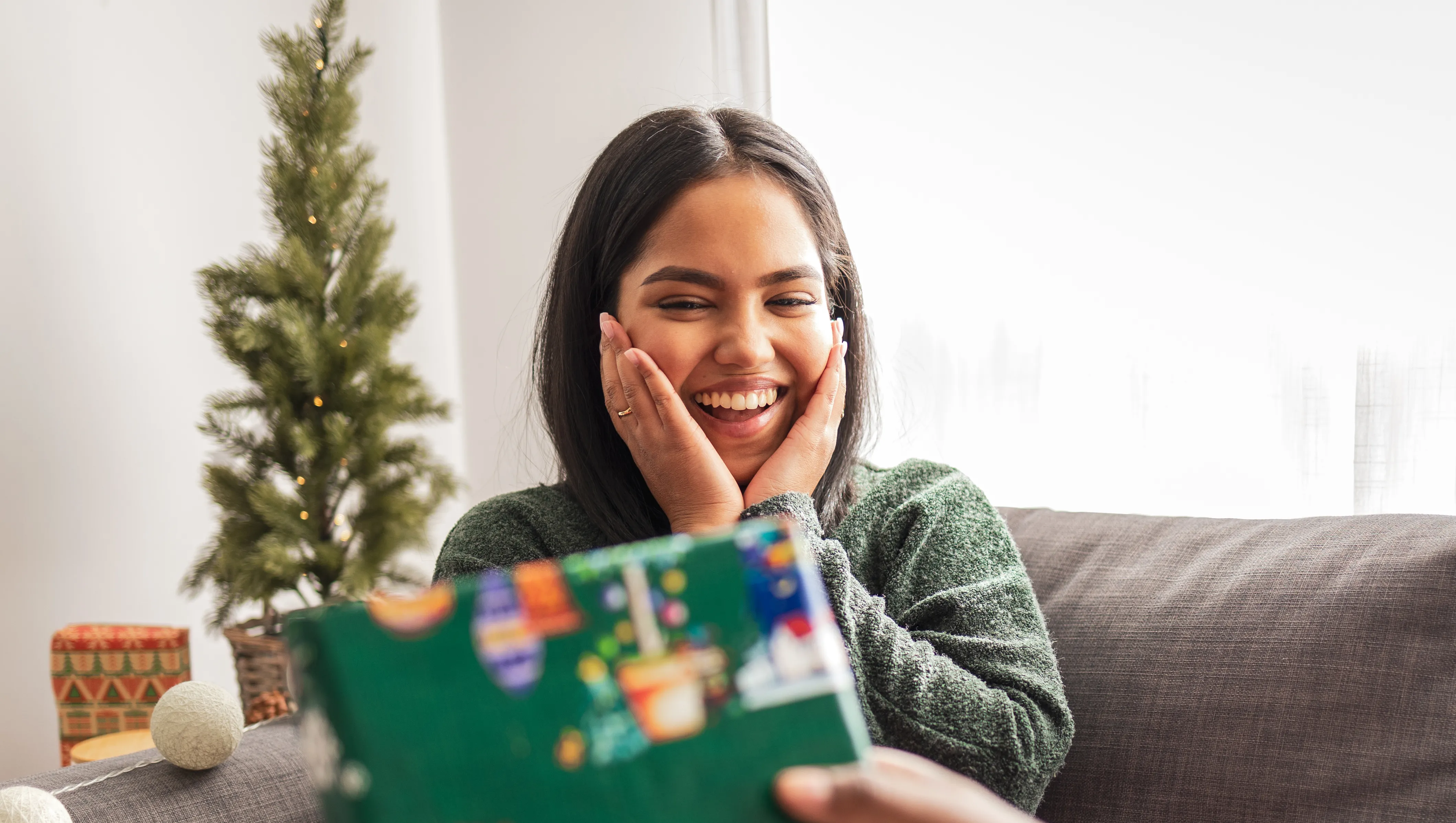 Young woman sitting on the sofa. Her boyfriend is giving her a present for Christmas