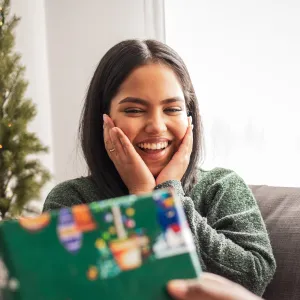 Young woman sitting on the sofa. Her boyfriend is giving her a present for Christmas