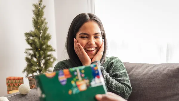 Young woman sitting on the sofa. Her boyfriend is giving her a present for Christmas
