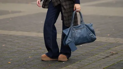 DUESSELDORF, GERMANY - OCTOBER 14: Evi Wave is seen wearing a navy blue and grey argyle knit H&M cardigan with a collared neckline, front button closure with tonal buttons and ribbed cuffs; some delicate chain and ball chain necklaces; a plaid Our Legacy overshirt in brown-based tartan pattern is tied around the waist; a pair of dark indigo wide-leg Closed jeans with a relaxed fit; her shoes are Chunky platform suede UGG mini boots in a camel-tan color; on her fingers she wears silver rings from Ariane Ernst and her nails are polished in red; she carries a navy blue Balenciaga Le City bag maxi in Arena Storico lambskin with two leather hand-braided handles, brass hardware, front zipped pocket and knotted leather puller; her brown hair is slicked back into a neat low bun; she wears a pair of cat-eye Prada sunglasses in tortoiseshell acetate with dark lenses; she wears a pair of sculptural beaded earrings handmade with white glass beads by Kroon02 on October 14, 2025 in Duesseldorf, Germany. (Photo by Moritz Scholz/Getty Images)