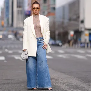 NEW YORK, NEW YORK - FEBRUARY 11: Merve Gorgotz wears sunglasses, earrings, a floral embroidery gray turtleneck top, a white oversized blazer jacket flared blue denim jeans pants , silver shoes, outside Area, during New York Fashion Week, on February 11, 2024 in New York City. (Photo by Edward Berthelot/Getty Images)