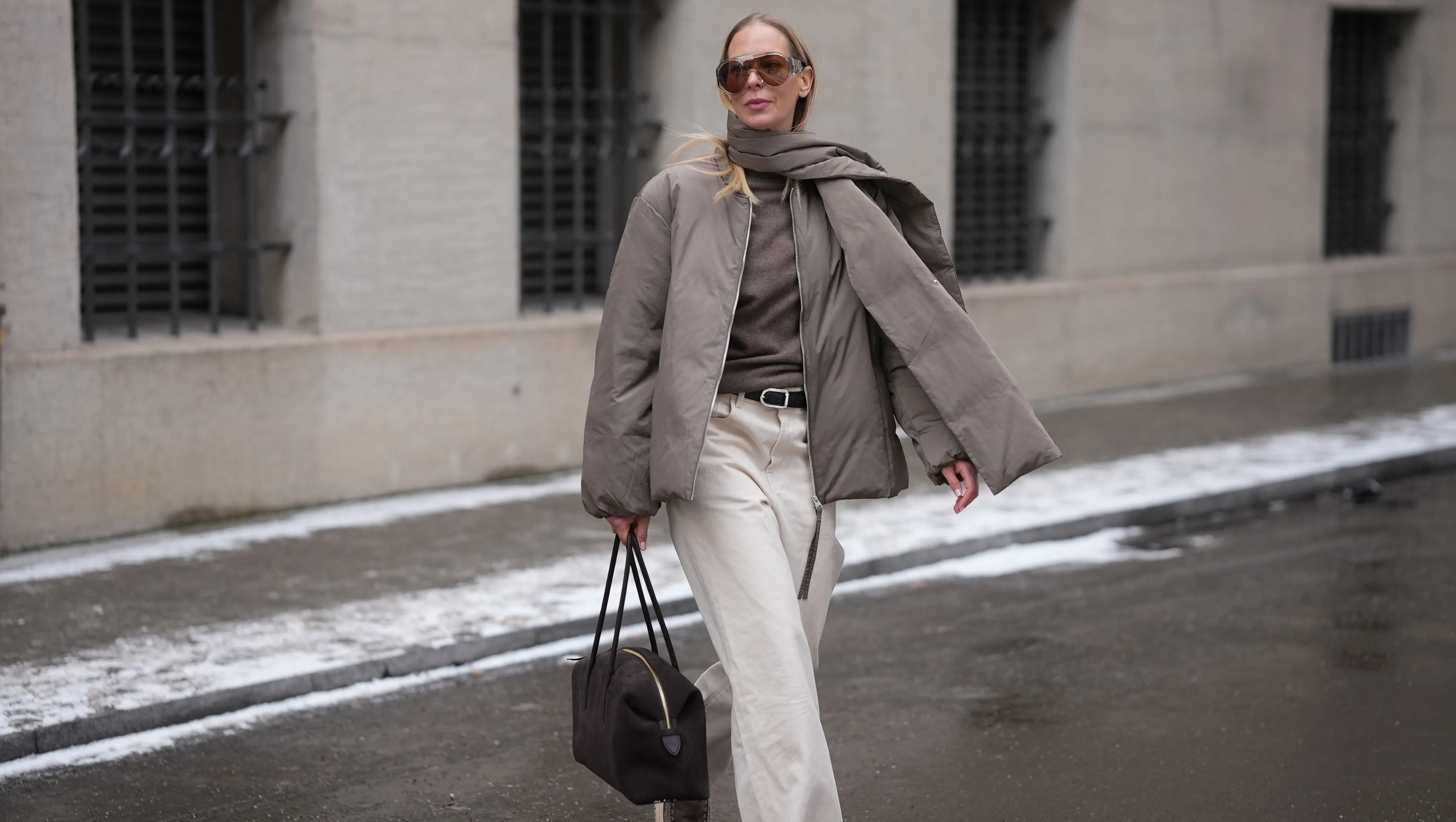 MUNICH, GERMANY - JANUARY 8: Mirja Klein is seen wearing a khaki padded jacket with an integrated scarf detail, a relaxed oversized silhouette and dropped shoulders from Arket; a brown cashmere knit sweater with a fine texture and classic crew neckline from Jacquemus; off white straight leg jeans with a high rise and structured cotton fabric from R&oacute;he Frames; a black leather belt with a metal buckle from Dehanche; a brown suede leather shoulder bag with a minimalist rectangular shape, top zipper and slim shoulder straps from Demellier London; oversized aviator style sunglasses with brown tinted lenses and a clear acetate frame from Bottega Veneta; her long blond straight hair is worn loose on January 8, 2026 in Munich, Germany. (Photo by Moritz Scholz/Getty Images)