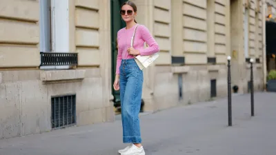 Diane Batoukina wears dark brown large squared sunglasses from Dior, a pale pink braided wool pullover from Ralph Lauren, blue faded denim / buttons high waist / wide legs pants, a white latte matte leather 30 Montaigne handbag from Dior, white suede and leather sneakers from Chanel, during a street style fashion photo session, on April 21, 2023 in Paris, France.
