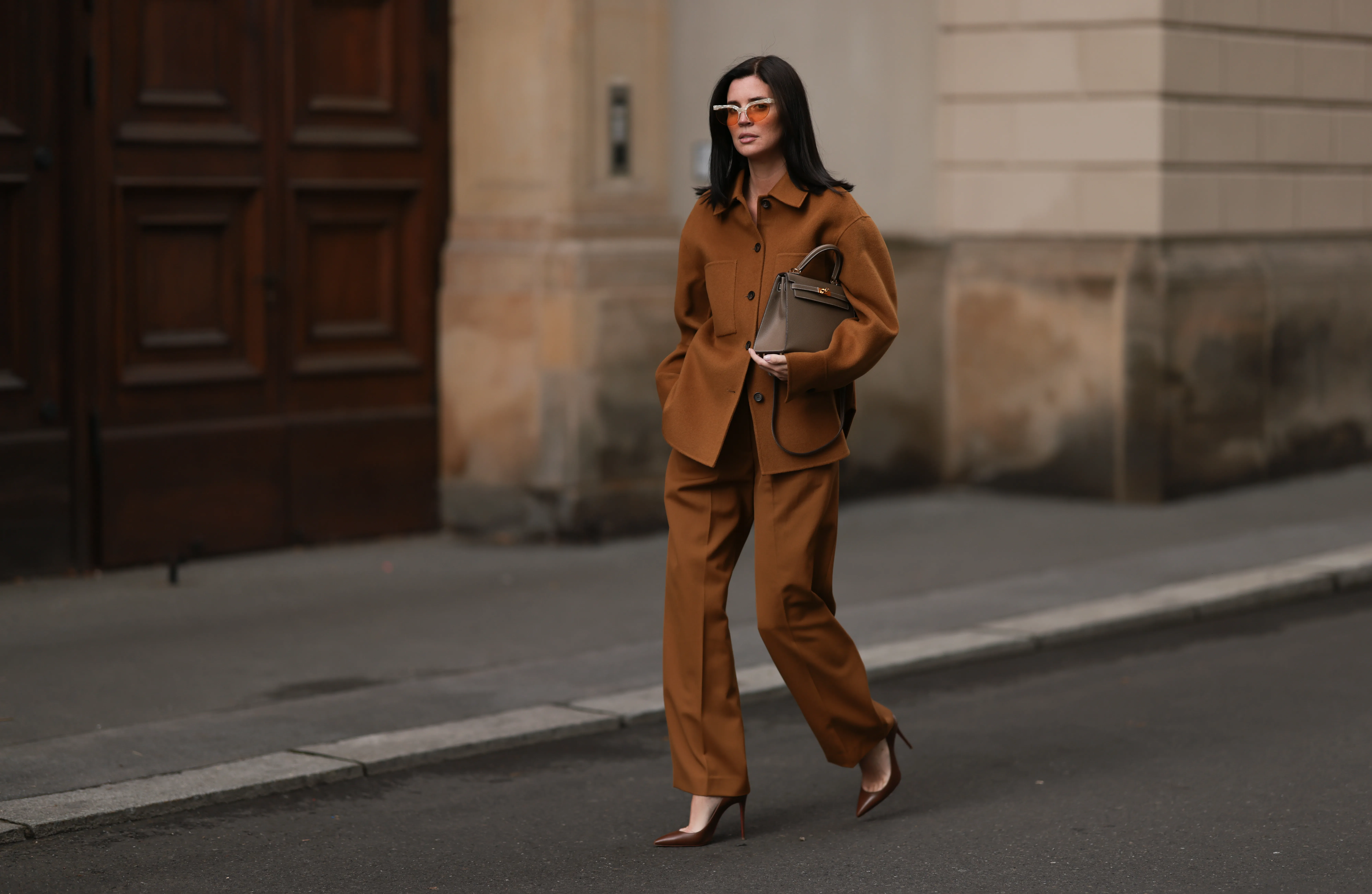 Leo Eberlin is seen wearing half-rimless cat-eye sunglasses with orange lenses and a grey structured top-frame from & Other Stories; a brown two-piece from Arket, consisting of a jacket with dark brown button placket, collar, and large chest pockets, a wide-legged pants with crease; a beige leather &ldquo;Kelly&ldquo; bag from Herm&egrave;s; and pointed brown leather high heels from Christian Loubouti on October 03, 2024 in Berlin, Germany.