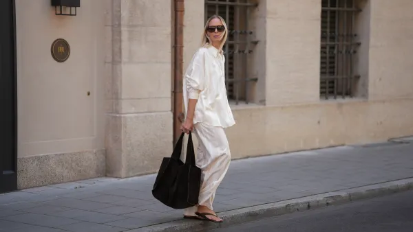 Mirja Klein is seen wearing a matching set consisting of a white striped oversized dobby-weave shirt with collar and buttons down in the front from H&M and a white striped straight pull-on trousers with loose fit and straight legs from H&M; a black suede tote bag with slouchy design and open top from COS; black oversized aviator sunglasses from Tom Ford; a pair of khaki green suede flip flops from A.EMERY on June 18, 2025 in Munich, Germany.