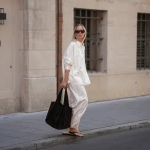 Mirja Klein is seen wearing a matching set consisting of a white striped oversized dobby-weave shirt with collar and buttons down in the front from H&M and a white striped straight pull-on trousers with loose fit and straight legs from H&M; a black suede tote bag with slouchy design and open top from COS; black oversized aviator sunglasses from Tom Ford; a pair of khaki green suede flip flops from A.EMERY on June 18, 2025 in Munich, Germany.