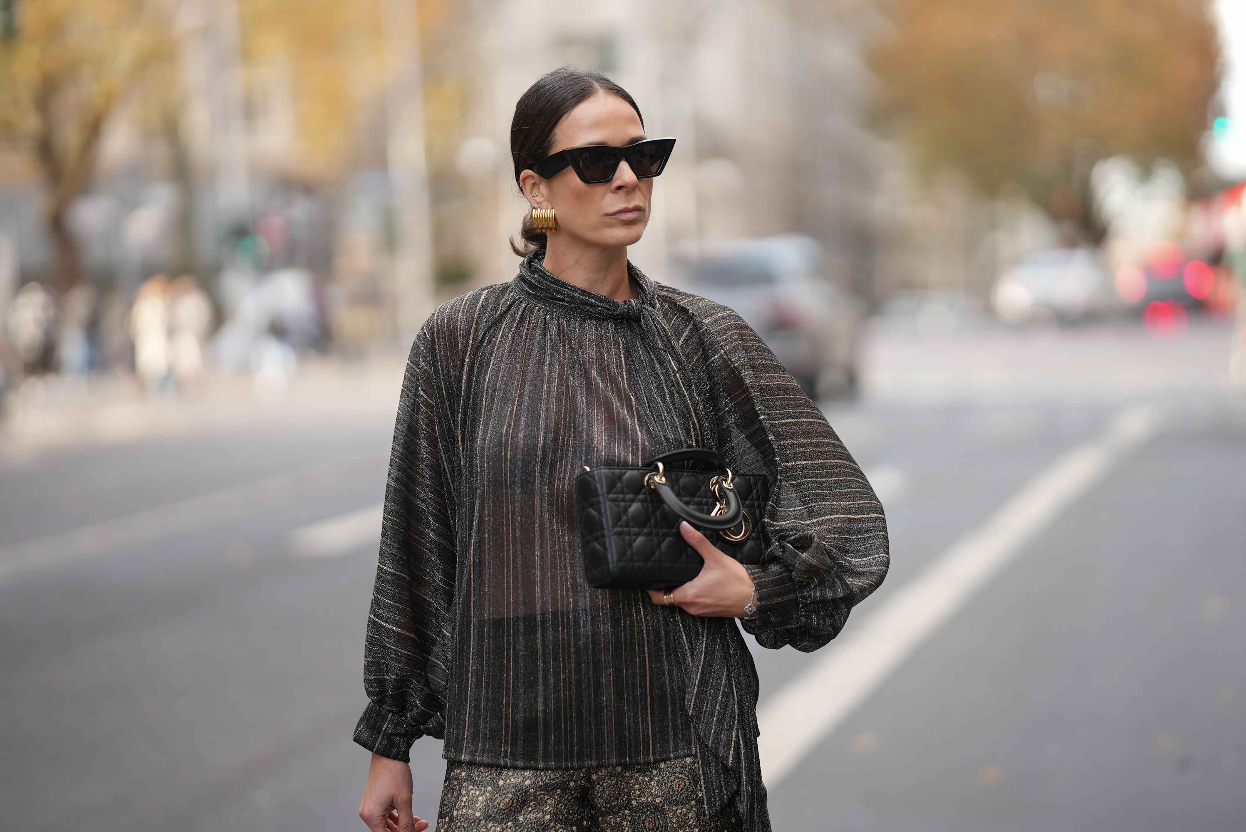 Patricia Wirschke is seen wearing a shimmering metallic striped blouse in shades of charcoal, bronze, and silver with a see through, flowing silhouette, high neckline and tie detail at the collar by Si Yu; paired with satin wide-leg trousers featuring an intricate geometric print in gold and dark brown tones by Si Yu; a small black quilted leather &ldquo;Lady D-Joy&rdquo; handbag with gold hardware by Dior; black cat-eye sunglasses with a chunky rim by Phoebe Philo; gold statement hoop earrings by an unknown brand; a rose gold &ldquo;B.zero1&rdquo; ring by Bulgari; a white gold &ldquo;Alhambra&rdquo; bracelet by Van Cleef & Arpels; her brown hair is in a sleek low bun parted in the middle on November 10, 2025 in Duesseldorf, Germany.
