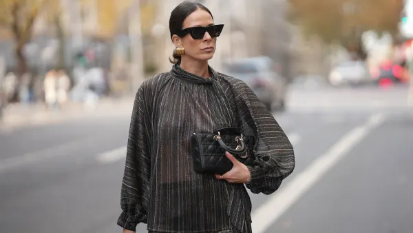 Patricia Wirschke is seen wearing a shimmering metallic striped blouse in shades of charcoal, bronze, and silver with a see through, flowing silhouette, high neckline and tie detail at the collar by Si Yu; paired with satin wide-leg trousers featuring an intricate geometric print in gold and dark brown tones by Si Yu; a small black quilted leather “Lady D-Joy” handbag with gold hardware by Dior; black cat-eye sunglasses with a chunky rim by Phoebe Philo; gold statement hoop earrings by an unknown brand; a rose gold “B.zero1” ring by Bulgari; a white gold “Alhambra” bracelet by Van Cleef & Arpels; her brown hair is in a sleek low bun parted in the middle on November 10, 2025 in Duesseldorf, Germany.