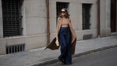 MUNICH, GERMANY - OCTOBER 28: Annette Weber is seen wearing a long camel sleeveless wool coat with wide notch lapels, oversized patch pockets and a fluid silhouette from Max Mara; a fitted camel rib-knit turtleneck body with a fine vertical texture from Max Mara; dark blue wide leg denim pants with a high waist and a structured drape from Max Mara; black patent boots with a shiny finish and chunky heel from Jimmy Choo; a small cream structured leather bag featuring a small top handle, gold zip closure and a minimal trapeze silhouette from Loro Piana; oversized black sunglasses with a bold shield frame and dark lenses from Gucci; large sculptural gold-tone statement earrings with organic round shapes from Max Mara; her brown hair is worn straight and middle parted on October 28, 2025 in Munich, Germany. (Photo by Moritz Scholz/Getty Images)