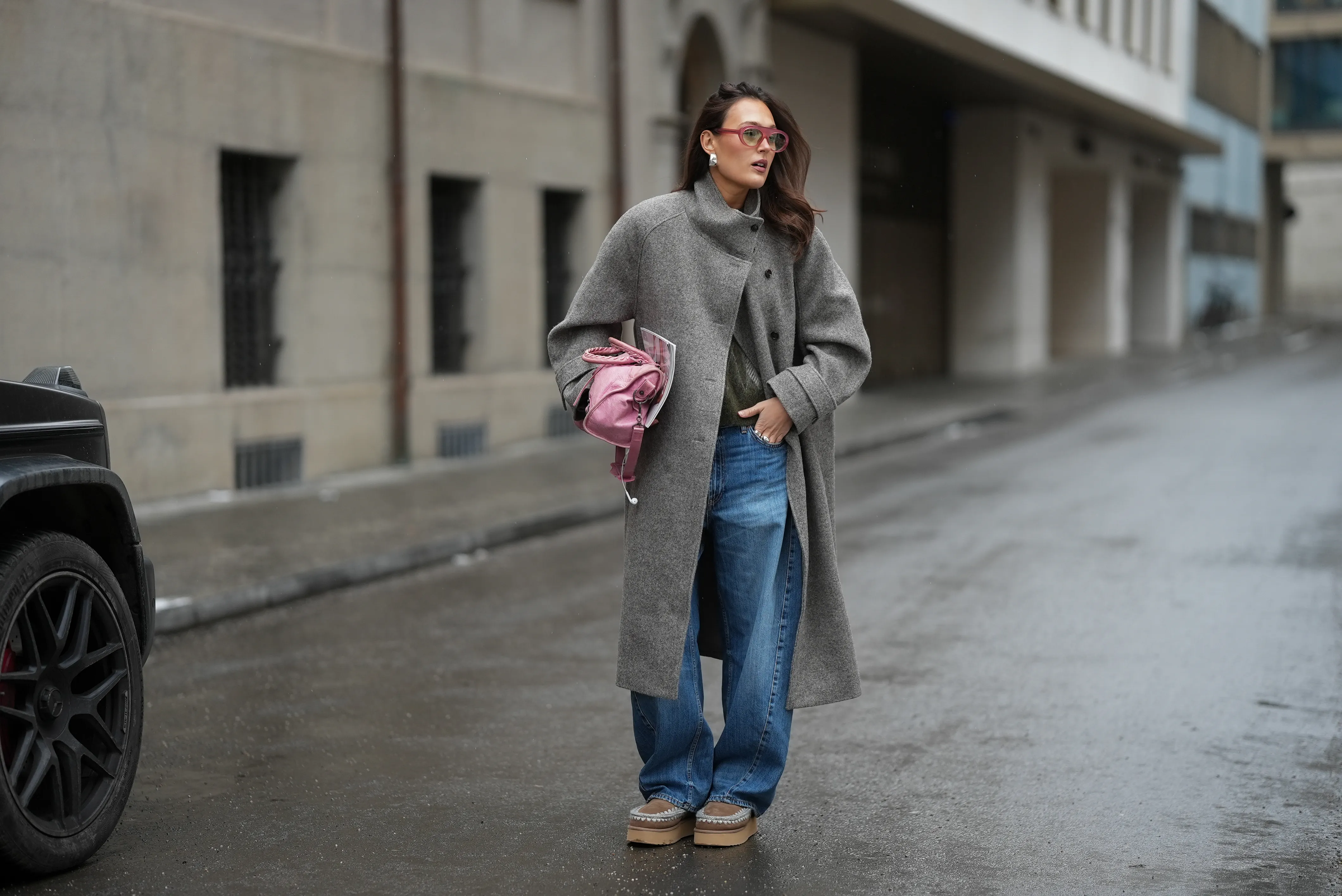 Amanda M&uuml;hle is seen wearing a grey wool coat with wide lapels, button closure and buttoned collar from Siyazu; a patterned knit sweater in muted green and pink tone with a argyle pattern and soft wool blend texture from Marc O&rsquo;Polo Denim; a white cotton base layer T-shirt from COS worn underneath; blue denim jeans with a loose straight leg cut from Zara; beige suede Mou boots with a platform sole and signature stitched detailing from Mou; a pink leather Balenciaga &ldquo;City bag&rdquo; with a softly slouched shape, top handles and silver hardware from Balenciaga; multiple silver rings from Pilgrim; holding a Vogue Magazine; aviator style glasses with a pink tinted frame and slightly tinted lenses from Lexxola; silver statement earrings with a sculptural finish from Mango; her long brown hair is worn loose and side parted on January 8, 2026 in Munich, Germany.