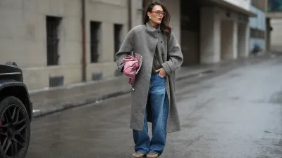 Amanda Mühle is seen wearing a grey wool coat with wide lapels, button closure and buttoned collar from Siyazu; a patterned knit sweater in muted green and pink tone with a argyle pattern and soft wool blend texture from Marc O’Polo Denim; a white cotton base layer T-shirt from COS worn underneath; blue denim jeans with a loose straight leg cut from Zara; beige suede Mou boots with a platform sole and signature stitched detailing from Mou; a pink leather Balenciaga “City bag” with a softly slouched shape, top handles and silver hardware from Balenciaga; multiple silver rings from Pilgrim; holding a Vogue Magazine; aviator style glasses with a pink tinted frame and slightly tinted lenses from Lexxola; silver statement earrings with a sculptural finish from Mango; her long brown hair is worn loose and side parted on January 8, 2026 in Munich, Germany.
