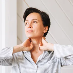 Portrait of young adult brunette woman doing facial massage with hands in bedroom at home, morning skincare routine
