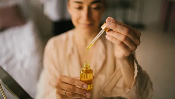 Portrait of beautiful young woman holding natural face oil. Beauty cosmetic concept.