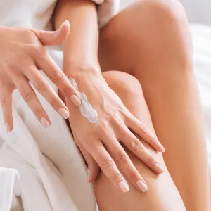 Take care. Happy young woman sitting on her bed and relaxing after shower while testing new cream