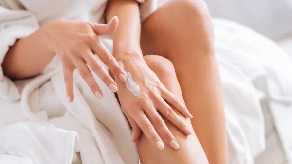 Take care. Happy young woman sitting on her bed and relaxing after shower while testing new cream