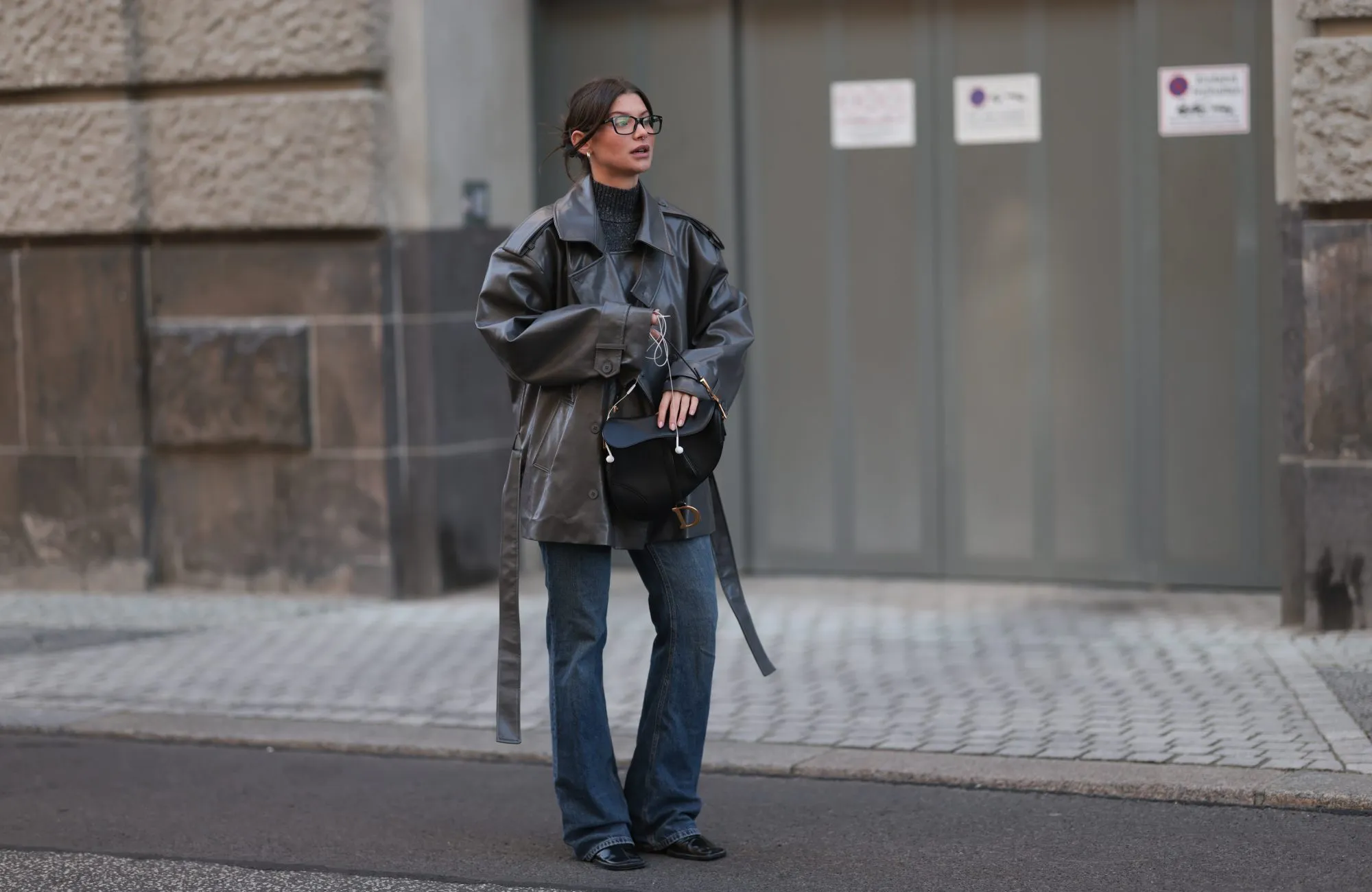 BERLIN, GERMANY - NOVEMBER 07: Sophia Geiss with brown hair seen wearing a long grey black leather coat from Source Unknown layered over a grey Zara pullover, styled with light blue Mango jeans and black Jil Sander boots. She accessorizes her look with a black Christian Dior Saddle bag featuring gold hardware and classic black Ray-Ban sunglasses on November 07, 2025 in Berlin, Germany. (Photo by Jeremy Moeller/Getty Images)