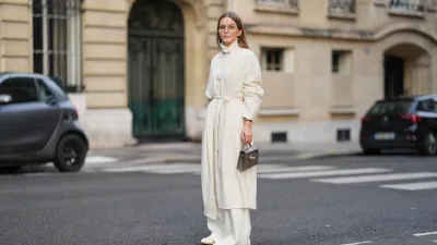 PARIS, FRANCE - DECEMBER 04: Diane Batoukina wears long light brown hair parted at the center with natural skin and neutral lipstick, a white cashmere long cardigan jacket by Lilysilk, a white cashmere turtleneck sweater by Bompard, white straight pants by Lilysilk, white leather loafers shoes by Baudoin and Lange, a grey Hermes Kelly 20 bag, during a street style fashion photo session, on December 04, 2025 in Paris, France, full body shot. (Photo by Edward Berthelot/Getty Images)