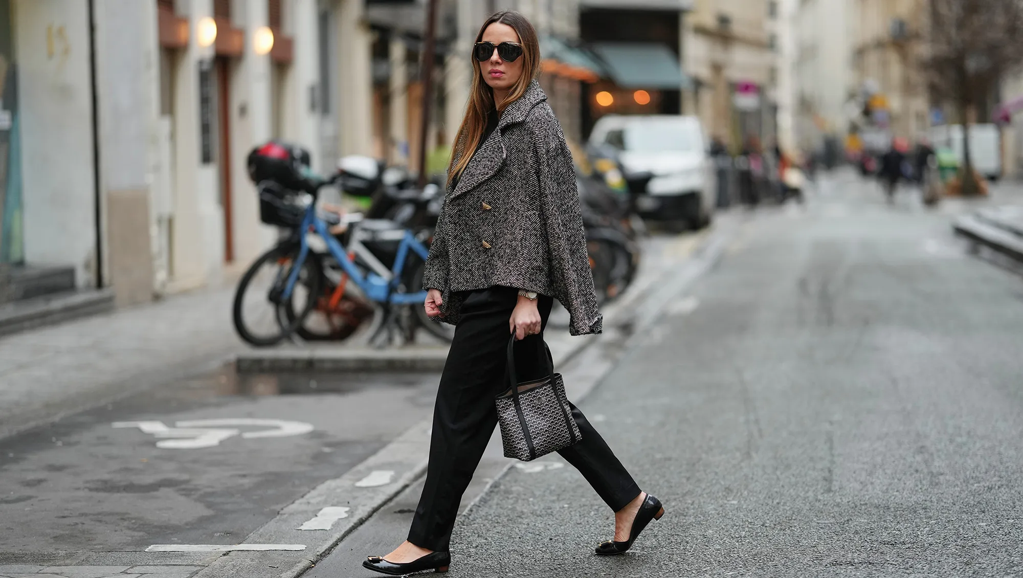PARIS, FRANCE - JANUARY 12: Maria Rosaria Rizzo wears long brown hair worn loose and parted at the center, Saint Laurent sunglasses with dark lenses, a black and white Pinel et Pinel bag with a structured rectangular shape in leather with printed monogram logo print and double top handles carried by hand, a black Marella knit sweater with a crew neckline, an Akep cropped jacket in a black and white textured pattern with wide lapels and front button fastening worn over the shoulders, black Balmain tailored pants with a straight leg, black leather Salvatore Ferragamo ballerina flats with a rounded toe, golden detail and low profile sole, during a street style fashion photo session, on January 12, 2026 in Paris, France. (Photo by Edward Berthelot/Getty Images)
