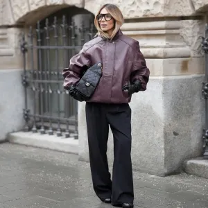 MUNICH, GERMANY - JANUARY 10: Oeznur Sinani alias Sinperi is seen wearing an oversized burgundy faux leather Prescott biker jacket with collar, hidden button front closure and minimalist design from The Frankie Shop; wide-leg black tailored trousers with relaxed fit from COS; black leather Tabi boots with flat sole and split toe from Maison Margiela; a black quilted grained calfskin leather Chanel 25 medium handbag with flap pockets, drawstring closing and golden chain strap and logo detail from Chanel; long black leather gloves from Mango; black oversized aviator glasses with black acetate frames and clear glasses from Prada; her blonde hair is styled in a blow out look on January 10, 2026 in Munich, Germany. (Photo by Moritz Scholz/Getty Images)