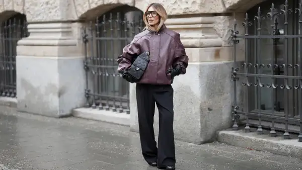 MUNICH, GERMANY - JANUARY 10: Oeznur Sinani alias Sinperi is seen wearing an oversized burgundy faux leather Prescott biker jacket with collar, hidden button front closure and minimalist design from The Frankie Shop; wide-leg black tailored trousers with relaxed fit from COS; black leather Tabi boots with flat sole and split toe from Maison Margiela; a black quilted grained calfskin leather Chanel 25 medium handbag with flap pockets, drawstring closing and golden chain strap and logo detail from Chanel; long black leather gloves from Mango; black oversized aviator glasses with black acetate frames and clear glasses from Prada; her blonde hair is styled in a blow out look on January 10, 2026 in Munich, Germany. (Photo by Moritz Scholz/Getty Images)