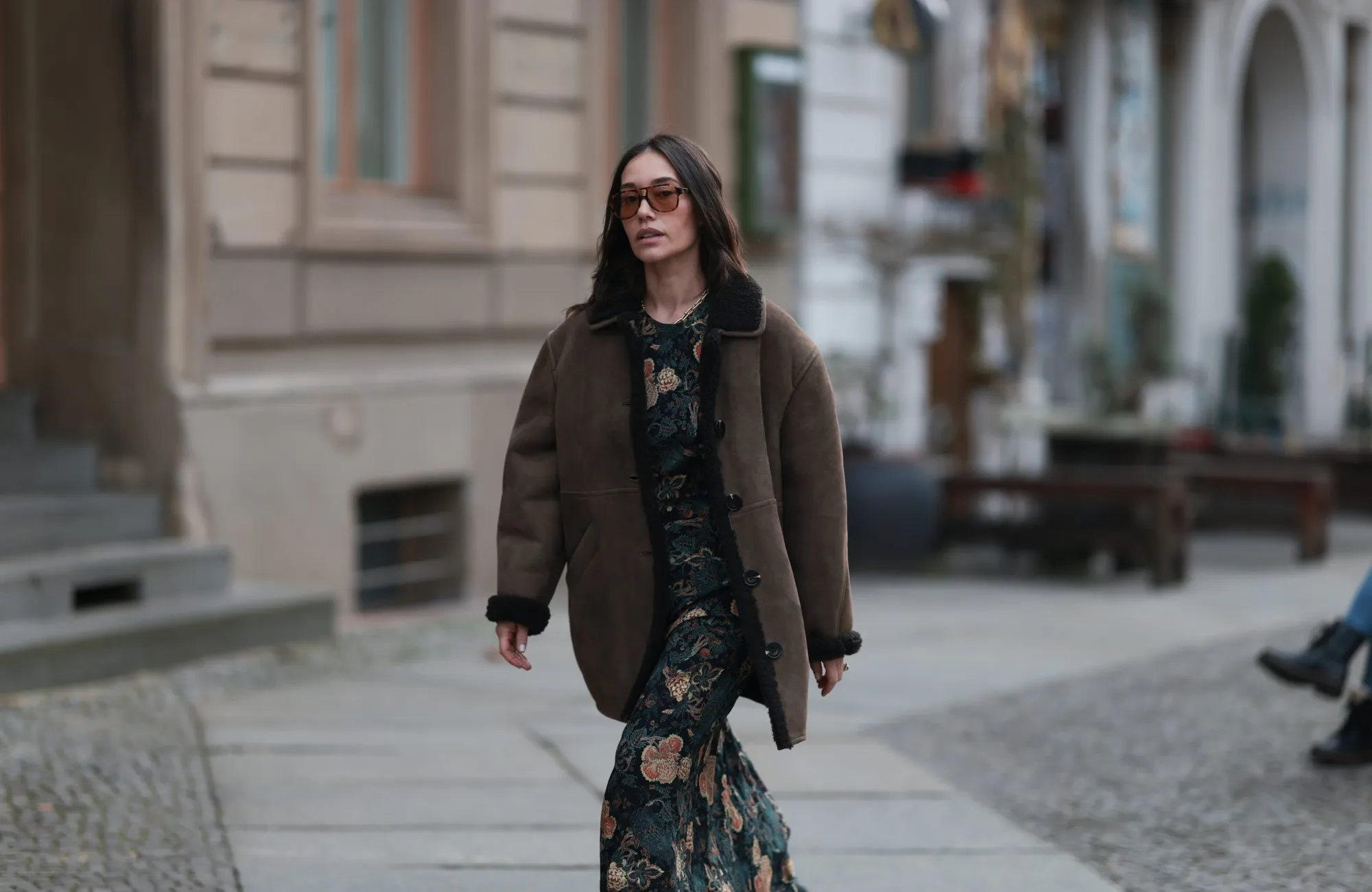 BERLIN, GERMANY - DECEMBER 04: Anna Sch&uuml;rrle seen wearing a brown shearling leather jacket by Soeur Paris layered over a long, floral-patterned Ulla Johnson dress. She completes the look with black Chanel leather boots and accessorizes with a yellow-gold chain necklace from the Tiffany & Co. City HardWear collection. She also wears oversized Corlin Eyewear sunglasses on December 04, 2025 in Berlin, Germany. (Photo by Jeremy Moeller/Getty Images)