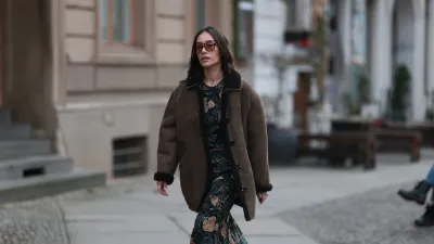 BERLIN, GERMANY - DECEMBER 04: Anna Schürrle seen wearing a brown shearling leather jacket by Soeur Paris layered over a long, floral-patterned Ulla Johnson dress. She completes the look with black Chanel leather boots and accessorizes with a yellow-gold chain necklace from the Tiffany & Co. City HardWear collection. She also wears oversized Corlin Eyewear sunglasses on December 04, 2025 in Berlin, Germany. (Photo by Jeremy Moeller/Getty Images)