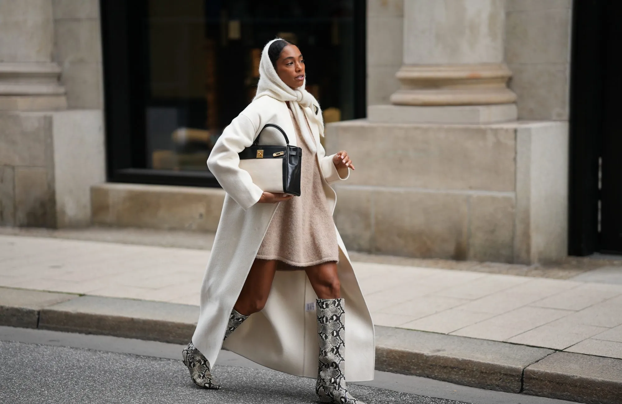 HAMBURG, GERMANY - OCTOBER 16: Cherifa Akili is seen wearing an oversized cream wool coat with a clean straight cut and dropped shoulders from Anine Bing; a wide beige knit sweater mini dress with a soft and fuzzy cashmere texture from by Aylin Koenig; cream knit headscarf in a fluffy mohair-blend from by Aylin Koenig; knee-high snake-embossed leather boots in a grey and black reptile pattern with a pointed toe from Arket; a structured two tone „Kelly bag“ with a structured black leather body, cream linen canvas front detailing and gold hardware from Hermés; her hair is styled slicked back with middle parting and partly covered by the hood-scarf on October 16, 2025 in Hamburg, Germany. (Photo by Moritz Scholz/Getty Images)
