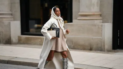 HAMBURG, GERMANY - OCTOBER 16: Cherifa Akili is seen wearing an oversized cream wool coat with a clean straight cut and dropped shoulders from Anine Bing; a wide beige knit sweater mini dress with a soft and fuzzy cashmere texture from by Aylin Koenig; cream knit headscarf in a fluffy mohair-blend from by Aylin Koenig; knee-high snake-embossed leather boots in a grey and black reptile pattern with a pointed toe from Arket; a structured two tone „Kelly bag“ with a structured black leather body, cream linen canvas front detailing and gold hardware from Hermés; her hair is styled slicked back with middle parting and partly covered by the hood-scarf on October 16, 2025 in Hamburg, Germany. (Photo by Moritz Scholz/Getty Images)