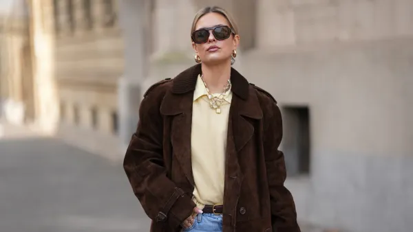 FRANKFURT AM MAIN, GERMANY - JANUARY 21: Julia Kammerer is seen wearing a long chocolate brown suede vintage trench coat with a wide lapel collar, button front and a relaxed fit; a butter yellow blouse with classic collar from JJXX; a light yellow knit sweater from H&M layered above the blouse; light blue wash jeans with turned up cuffs, straight leg and relaxed fit from Levi’s; a mocha brown suede leather Midi Hudson tote bag with top handle and adjustable belt from DeMellier; oversized aviator sunglasses with brown tortoiseshell frames and tinted lenses from H&M; a gold-plated brass necklace with natural freshwater pearls from Scandivv; a golden chain necklace with key lock pendant from MyJewellery; a golden chain necklace with „A“-letter pendant from Scandivv; chunky golden hoop earrings from COS; a slim brown leather belt with golden buckle from Lilysilk; Samba OG leather-trimmed leopard-print pony hair sneakers from Adidas x Wales Bonner; her blonde hair styled back on January 21, 2026 in Frankfurt am Main, Germany. (Photo by Moritz Scholz/Getty Images)