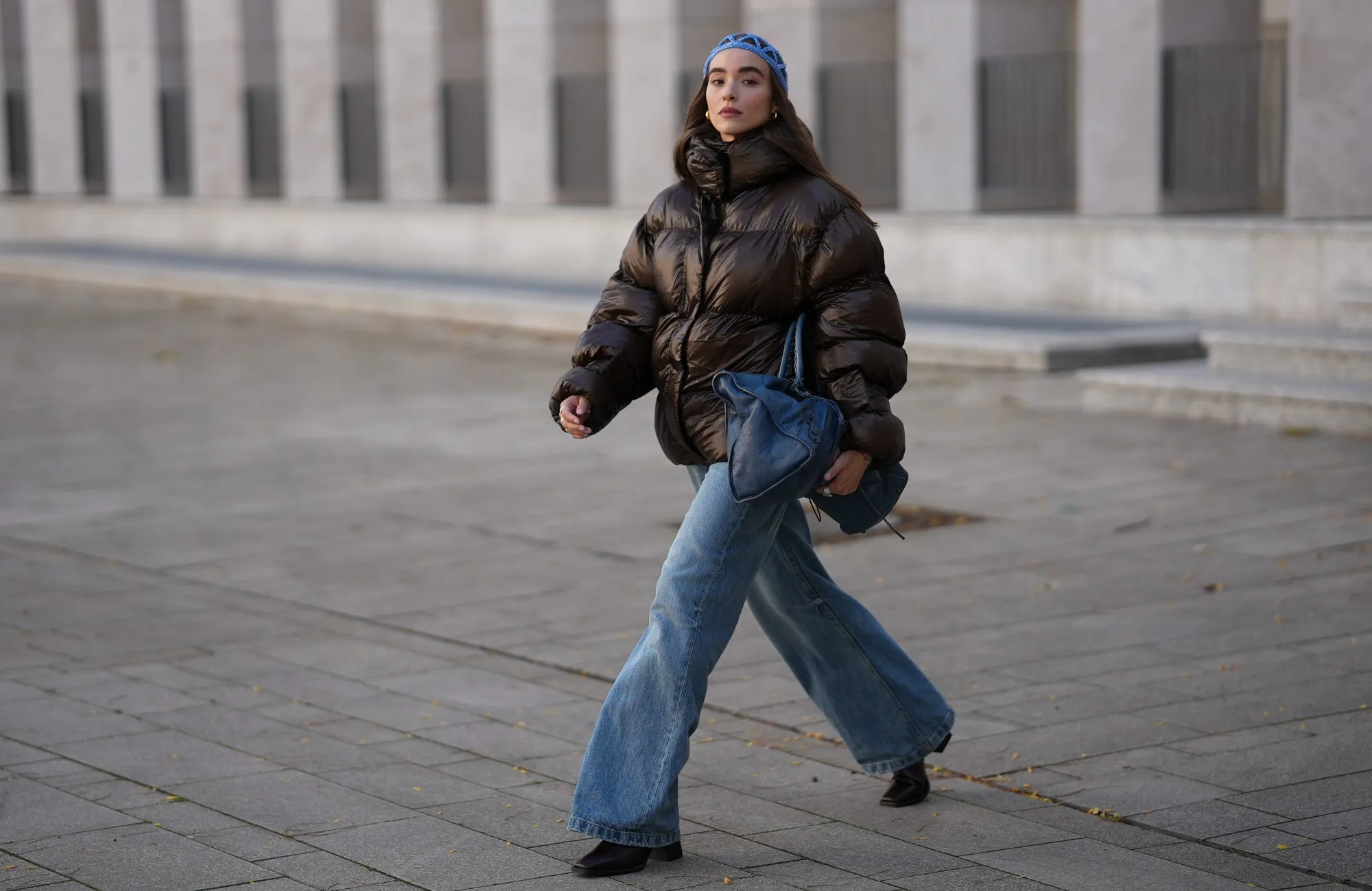COLOGNE, GERMANY - SEPTEMBER 18: Evi Wave is seen wearing a dark brown high-shine puffer jacket, oversized and voluminous with a high neckline from Oval Square; light blue wide-leg jeans, relaxed fit and slightly washed from Agolde; black square-toe boots with a chunky heel from Vagabond; the Motocross Classic Work, large slouchy blue leather bag with subtle details and seaming from Balenciaga; subtle silver rings from Ariane Ernst; an open blue crocheted beanie-style hat from Kroon02; her brown hair is worn loose on September 18, 2025 in Cologne, Germany. (Photo by Moritz Scholz/Getty Images)