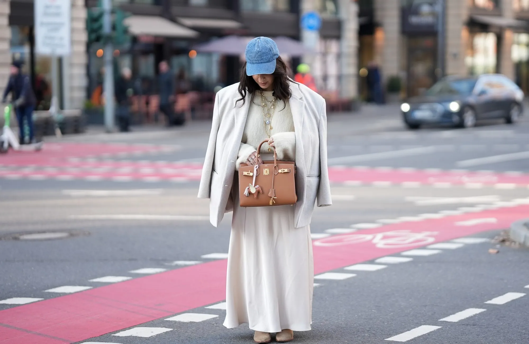 FRANKFURT AM MAIN, GERMANY - JANUARY 20: Cansu Yildirim is seen wearing a cream-coloured satin maxi skirt with flowing, slightly flared silhouette from Philosophy di Lorenzo Serafini; a cloud dancer white fuzzy knit pullover with relaxed fit from H&M tucked in the skirt; a light beige oversized single-breasted wool blazer from ASOS; taupe brown suede leather ankle boots with pointed toe and block heel from Massimo Dutti; a tan brown leather Kelly 25 bag with structured shape and gold hardware from Herm&egrave;s; a horse-shaped tan brown leather bag charm with light pink strap attached to the bag; a washed blue denim baseball cap from COS; layered golden chain necklaces with pearl pendants; her dark hair is styled in loose waves with a side parting on January 20, 2026 in Frankfurt am Main, Germany. (Photo by Moritz Scholz/Getty Images)