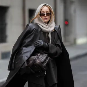 MUNICH, GERMANY - NOVEMBER 20: Anouk Delphine is seen wearing a long dark-brown leather coat with double breasted button fastening, structured shoulders and a straight cut, draped over the shoulders from H&M; an oversized dark-brown pinstriped blazer with notch lapels and a longline tailored silhouette from Zara; matching dark-brown pinstriped wide-leg trousers with a relaxed, slouchy drape from Zara; layered underneath is a dark-brown fine-knit cardigan in a soft wool blend from Allude; a vintage dark-brown quilted leather shoulder bag with silver-tone chain straps and an embossed logo from Chanel; black leather gloves in a smooth, fitted finish from Roeckl; slim rectangular acetate sunglasses with brown tinted lenses from Gucci; a soft beige alpaca-blend balaclava with an adjustable drawstring tie framing her face from Sézane; her blonde hair is worn straight with a center part and tucked loosely under the balaclava on November 20, 2025 in Munich, Germany. (Photo by Moritz Scholz/Getty Images)