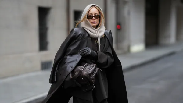 MUNICH, GERMANY - NOVEMBER 20: Anouk Delphine is seen wearing a long dark-brown leather coat with double breasted button fastening, structured shoulders and a straight cut, draped over the shoulders from H&M; an oversized dark-brown pinstriped blazer with notch lapels and a longline tailored silhouette from Zara; matching dark-brown pinstriped wide-leg trousers with a relaxed, slouchy drape from Zara; layered underneath is a dark-brown fine-knit cardigan in a soft wool blend from Allude; a vintage dark-brown quilted leather shoulder bag with silver-tone chain straps and an embossed logo from Chanel; black leather gloves in a smooth, fitted finish from Roeckl; slim rectangular acetate sunglasses with brown tinted lenses from Gucci; a soft beige alpaca-blend balaclava with an adjustable drawstring tie framing her face from Sézane; her blonde hair is worn straight with a center part and tucked loosely under the balaclava on November 20, 2025 in Munich, Germany. (Photo by Moritz Scholz/Getty Images)