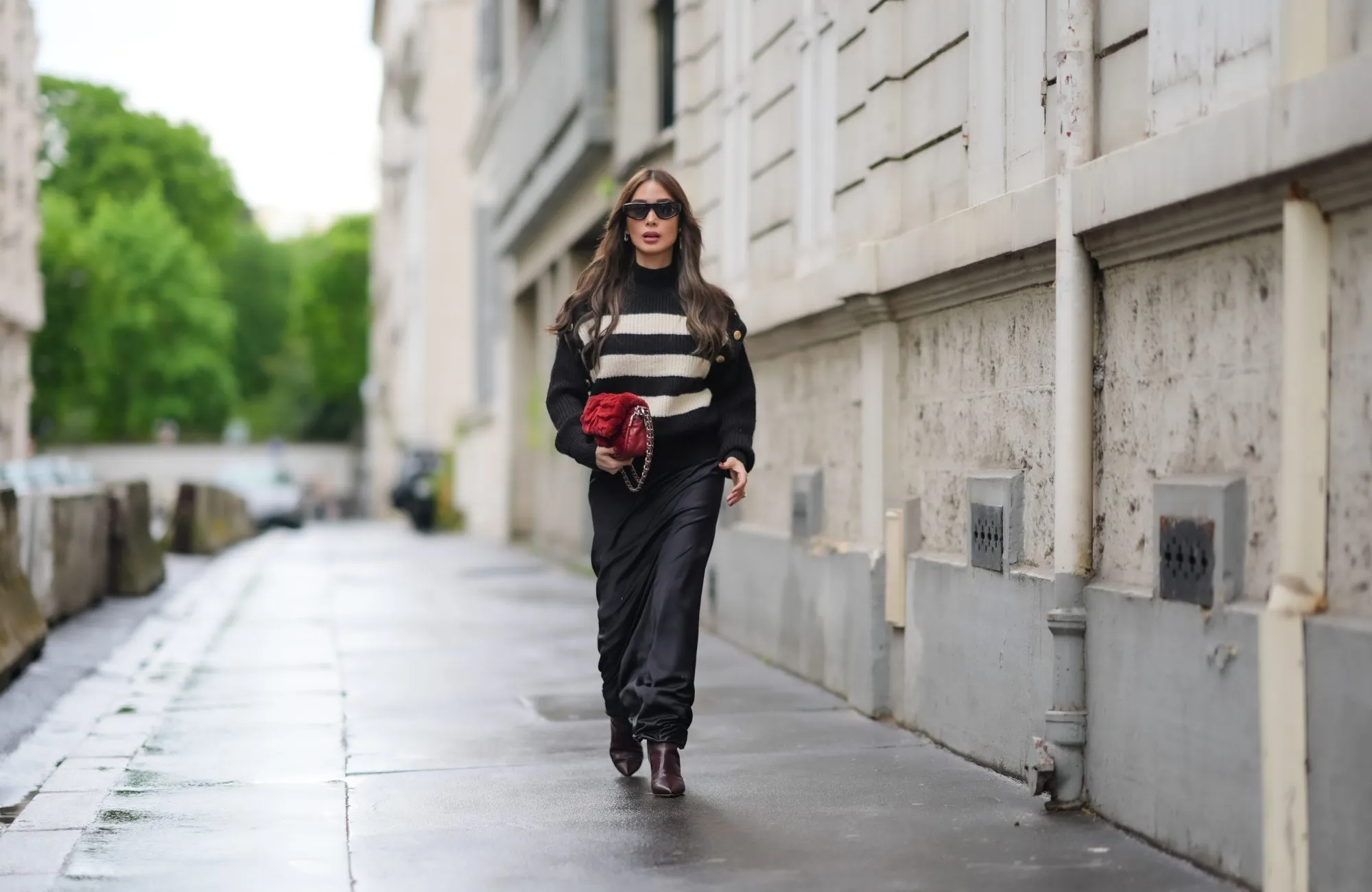 PARIS, FRANCE - APRIL 27: Heart Evangelista wears sunglasses, a black and white striped ribbed turtleneck pullover with golden buttons on the shoulders, a red fluffy Chanel bag, a black satin silky lustrous flowing skirt , brown pointed boots, during a street style fashion photo session, on April 27, 2024 in Paris, France. (Photo by Edward Berthelot/Getty Images)