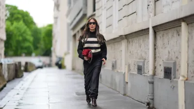 PARIS, FRANCE - APRIL 27: Heart Evangelista wears sunglasses, a black and white striped ribbed turtleneck pullover with golden buttons on the shoulders, a red fluffy Chanel bag, a black satin silky lustrous flowing skirt , brown pointed boots, during a street style fashion photo session, on April 27, 2024 in Paris, France. (Photo by Edward Berthelot/Getty Images)