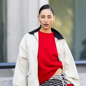 PARIS, FRANCE - OCTOBER 07: A guest wears a red sweater, a black and white striped asymmetrical skirt, gold heeled sandals and a beige and black jacket outside Christopher Esber show during the Womenswear Spring Summer 2026 as part of Paris Fashion Week on October 07, 2025 in Paris, France. (Photo by Valentina Frugiuele/Getty Images)