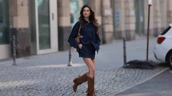 BERLIN, GERMANY - MARCH 21: Celine Bethmann seen wearing Cie Cie oversized dark-wash denim button-up western-inspired shirt with a relaxed fit, matching Cie Cie high-waisted dark blue denim mini skirt, vintage brown / tan suede leather handbag with braided handles and fringe elements and Steve Madden brown suede leather statement knee-high suede boots with fringe elements, on March 21, 2025 in Berlin, Germany. (Photo by Jeremy Moeller/Getty Images)