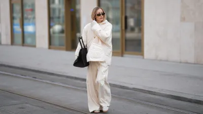 MUNICH, GERMANY - JANUARY 22: Anouk Delphine is seen wearing a thin cloud dancer white quilted puffer jacket with button front and oversized fit from The Frankie Shop; a cream white lace-trimmed top with asymmetric hemline from Zara; a cream knit sweater with hood from Windsor; off-white wide-leg trousers with vertical seam details and flared hems from H&M; slim sunglasses with black acetate frame and dark tinted lenses from Gucci; a black suede leather tote bag with top handles and slightly trapezoidal from COS; white Samba OG suede sneakers with black stripes from Adidas; her blonde hair is worn straight and parted in the middle on January 22, 2026 in Munich, Germany. (Photo by Moritz Scholz/Getty Images)
