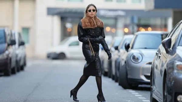 PARIS, FRANCE - DECEMBER 27: Emy Venturini wears dark brown hair parted at the center and pulled back with loose strands framing the face, natural makeup with an even complexion, defined brows and neutral-toned pale pink lipstick, black vintage leather dress coat by Saint Laurent with a fitted silhouette, front slit and brown fur-trimmed collar, sheer black tights by Calzedonia, black leather pumps shoes by Miu Miu with a pointed toe, black leather shoulder bag by Saint Laurent with a gold chain strap and embossed star patterns, black leather gloves by Saint Laurent, round black sunglasses by Ray-Ban, during a street style fashion photo session, on December 27, 2025 in Paris, France. (Photo by Edward Berthelot/Getty Images)