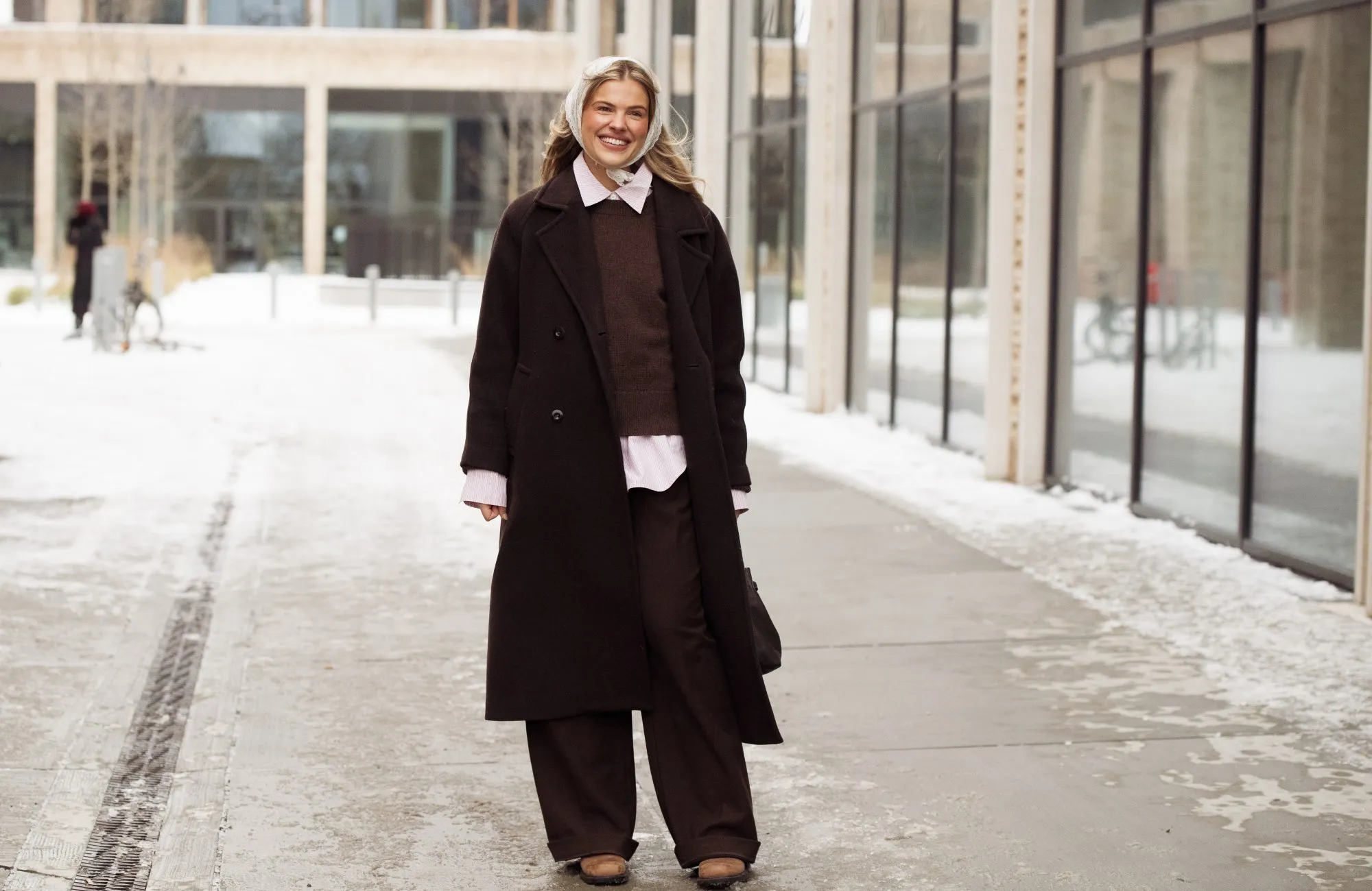 COPENHAGEN, DENMARK - JANUARY 28: Emma Stallmark wears a dark brown oversized wool overcoat layered over a brown knitted sweater and a pale pink button-down shirt with visible cuffs and hem, paired with wide-leg dark brown tailored trousers, brown leather shoes, a delicate gold necklace, a white lace headscarf tied under the chin, and carries a dark brown leather shoulder bag outside the Herskind show during Copenhagen Fashion Week AW26 on January 28, 2026 in Copenhagen, Denmark. (Photo by Raimonda Kulikauskiene/WireImage)