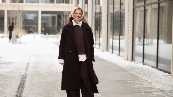 COPENHAGEN, DENMARK - JANUARY 28: Emma Stallmark wears a dark brown oversized wool overcoat layered over a brown knitted sweater and a pale pink button-down shirt with visible cuffs and hem, paired with wide-leg dark brown tailored trousers, brown leather shoes, a delicate gold necklace, a white lace headscarf tied under the chin, and carries a dark brown leather shoulder bag outside the Herskind show during Copenhagen Fashion Week AW26 on January 28, 2026 in Copenhagen, Denmark. (Photo by Raimonda Kulikauskiene/WireImage)