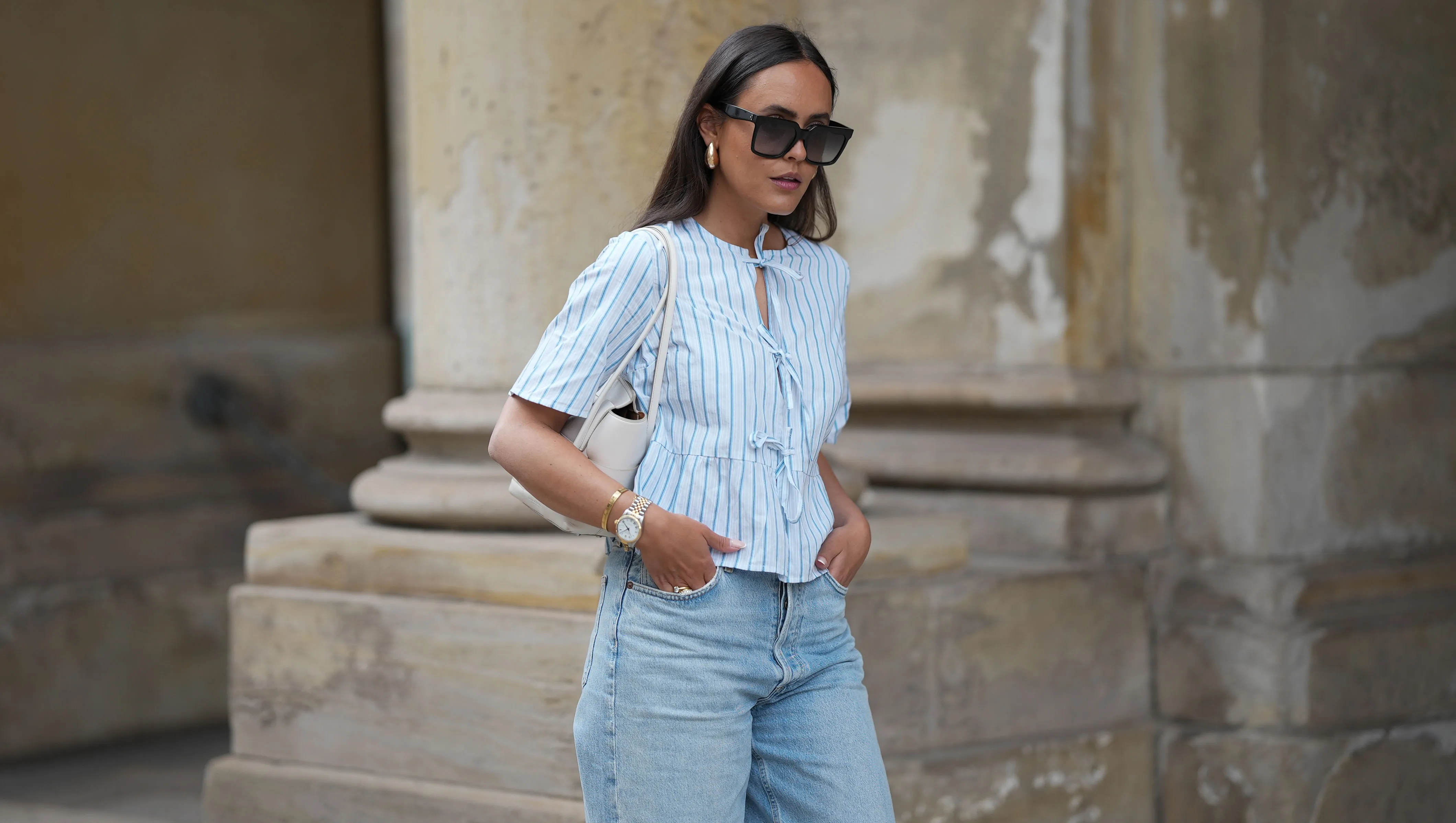 HAMBURG, GERMANY - MAY 7: Laura Noltemeyer is seen wearing a light indigo blue wide leg jeans from Agolde, a cotton puff sleeve blouse with ties in the front in white with blue stripes from S&eacute;zane, black oversized cat-eye acetate sunglasses from Celine, Arco handbag in white intrecciato leather from Bottega Veneta, big golden drop-shaped earrings, a small Lady-Datejust watch in gold-silver from Rolex, a golden LOVE bracelet from Cartier, stacked golden rings from Cartier on May 7, 2025 in Hamburg, Germany. (Photo by Moritz Scholz/Getty Images)