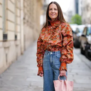 PARIS, FRANCE - APRIL 21: Alba Garavito Torre wears gold and black embossed pattern earrings, a camel with beige / blue / green / pink flower print pattern high neck / puffy long sleeves blouse from The Label Edition, high waist blue denim wide legs pants, gold rings, a pale pink matte leather handbag from Saonara Brand, beige matte leather pointed heels shoes, during a street style fashion photo session, on April 21, 2023 in Paris, France. (Photo by Edward Berthelot/Getty Images)