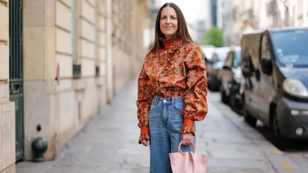 PARIS, FRANCE - APRIL 21: Alba Garavito Torre wears gold and black embossed pattern earrings, a camel with beige / blue / green / pink flower print pattern high neck / puffy long sleeves blouse from The Label Edition, high waist blue denim wide legs pants, gold rings, a pale pink matte leather handbag from Saonara Brand, beige matte leather pointed heels shoes, during a street style fashion photo session, on April 21, 2023 in Paris, France. (Photo by Edward Berthelot/Getty Images)