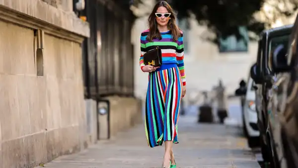Therese Hellström @tesshell wears white cat-eye sunglasses, a multi colored striped wool midi dress with long sleeves, a brown leather Hermes bag, green pointed shoes with metallic pearls, on April 08, 2021 in Paris, France.