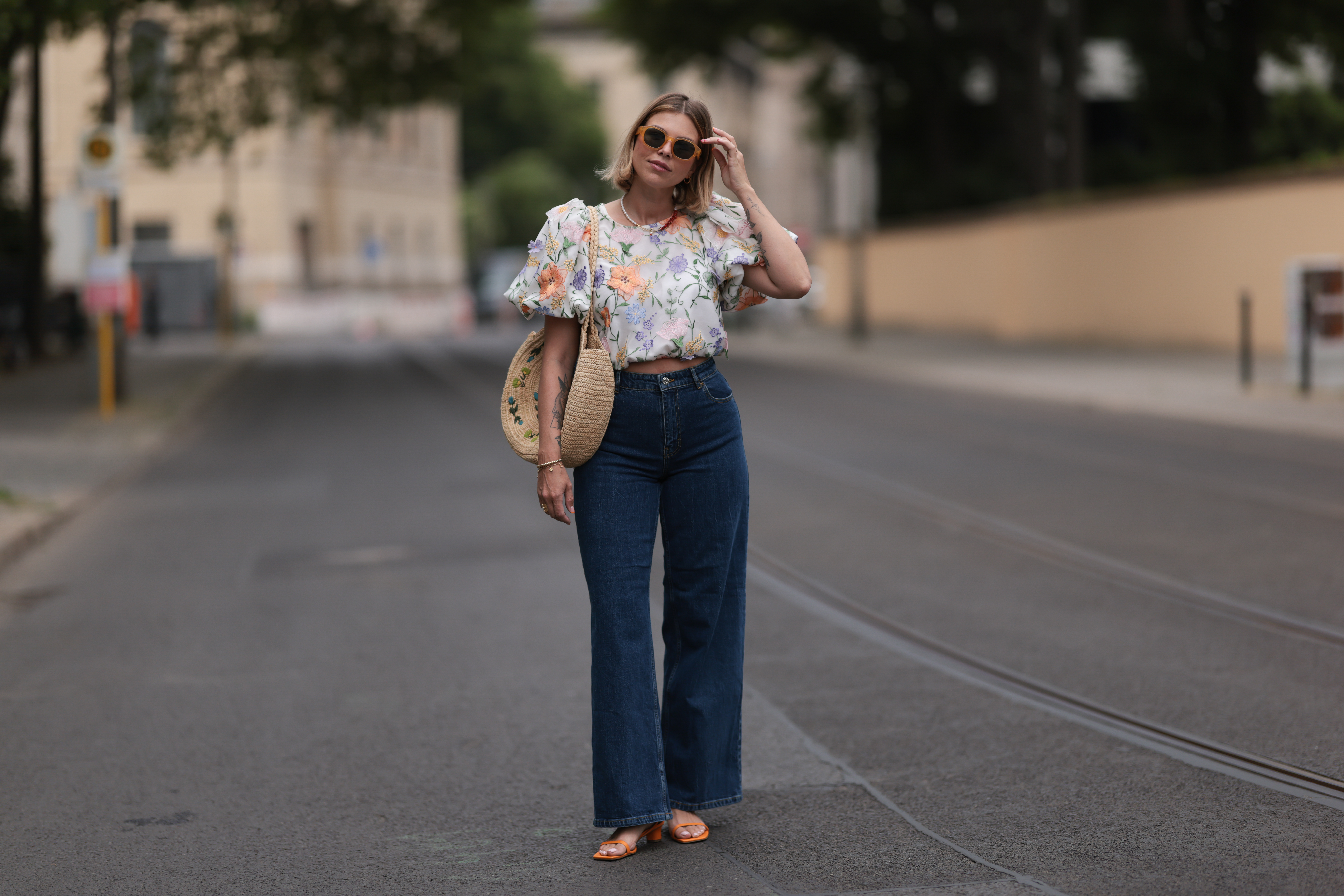Aline Kaplan wearing Baum & Pferdgarten wide leg blue denim pants, & other stories white flower pattern cropped blouse and orange summer heels and Mango orange black shades on June 06, 2023 in Berlin, Germany.